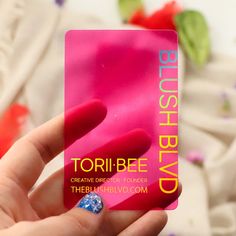 a person holding up a pink business card with blue and white designs on it's fingers