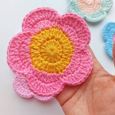 crocheted flower being held by someone's hand in front of them on a white surface