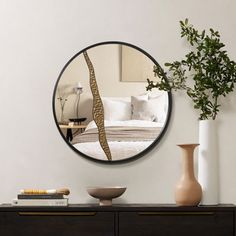 a round mirror on the wall above a dresser with vases and other items in front of it