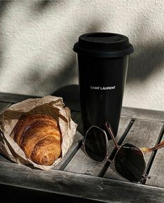 a croissant, coffee and sunglasses on a wooden table