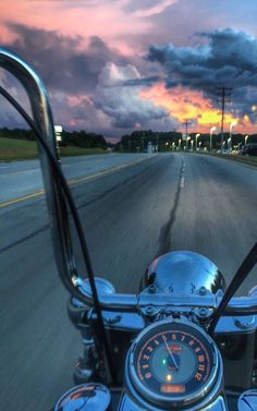 a motorcycle is driving down the road at sunset or dawn with clouds in the background