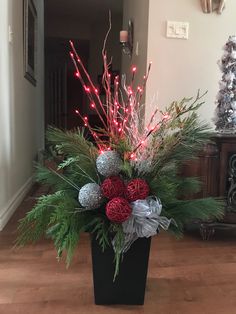 a christmas arrangement in a black vase with red and silver balls, greenery and lights