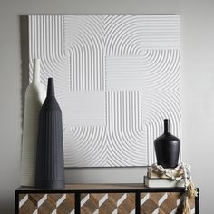 two vases are sitting on top of a dresser next to a white wall with an abstract design