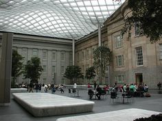 people are sitting and walking around in an open area with a glass roof over the courtyard