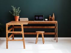 a wooden desk with a clock on it next to a chair and potted plant