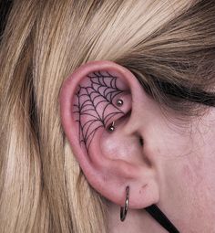 a woman's ear has a spider web tattoo on it