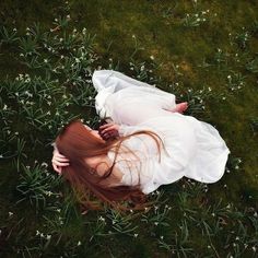 a woman laying in the grass with her head on her hands and arms behind her back