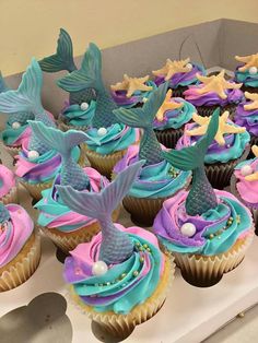 cupcakes decorated with blue, pink and purple icing are displayed on a table