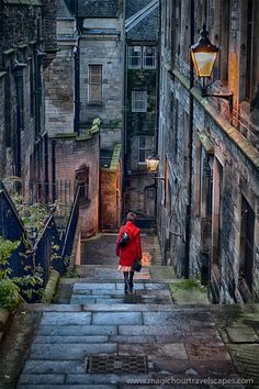 a woman walking up some steps in an alley way with buildings on both sides and a street light above her