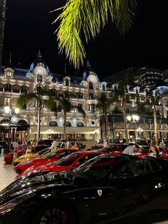 a bunch of cars are parked in front of a building at night with palm trees