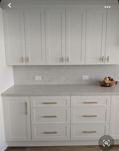 a white kitchen with marble counter tops and gold pulls on the cabinet doors is shown