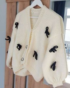 a white sweater with black appliques hanging on a door