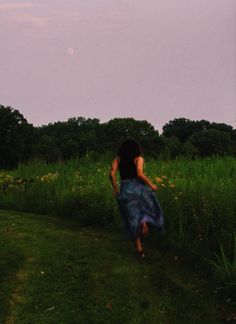 a woman in a blue dress is walking through the grass