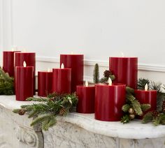 red candles are lined up on a mantle with pine cones and greenery around them