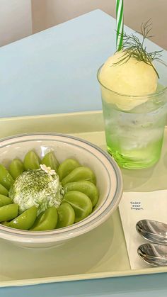 a bowl filled with green vegetables next to a drink on top of a tray covered in silverware