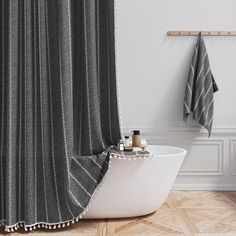 a bath tub sitting next to a shower curtain in a bathroom with wooden floors and white walls