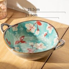 a bowl with flowers on it sitting on a wooden table next to a measuring tape