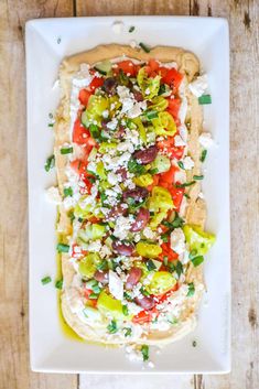 a white plate topped with an open pita bread covered in veggies and feta cheese