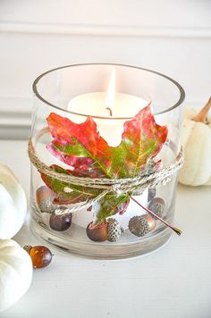 a candle that is sitting in a glass bowl with leaves and acorns around it