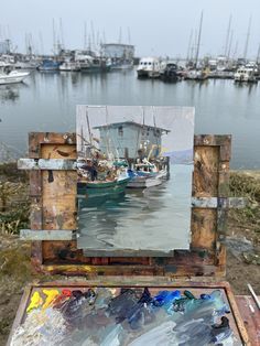 an artist's easel with a painting on it and boats in the water