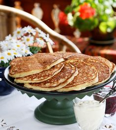 a stack of pancakes sitting on top of a cake plate next to a glass of milk