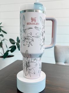 a white and blue coffee cup sitting on top of a wooden table next to a potted plant