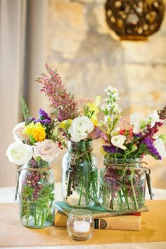 three mason jars filled with flowers sitting on top of a table next to an open book