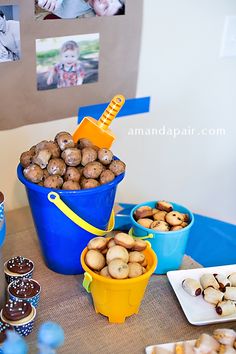 a table topped with blue buckets filled with food next to pictures on the wall