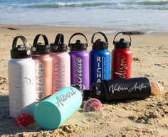 the water bottles are lined up on the sand near the ocean and seashells