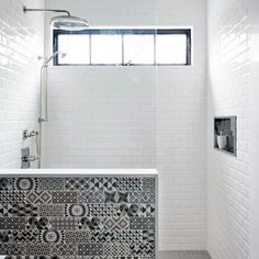 a white tiled bathroom with black and white tiles on the shower wall, tub, and window