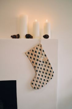 a christmas stocking hanging on the wall next to three candles and a fire place