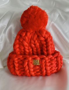 an orange knitted hat sitting on top of a white bed sheet with a tag