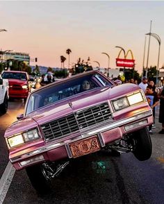 a pink car is parked on the side of the road in front of some people