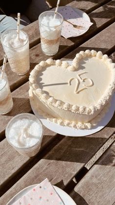 a heart shaped cake sitting on top of a wooden table next to cups and plates