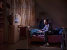 a man sitting on top of a bed next to a tv in a dark room