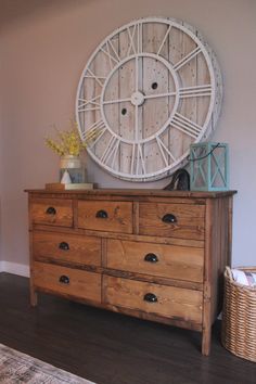 a wooden dresser with drawers and a large clock on the wall above it's head