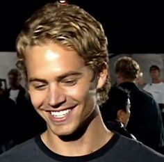 a man with blonde hair smiling and wearing a black t - shirt at an event