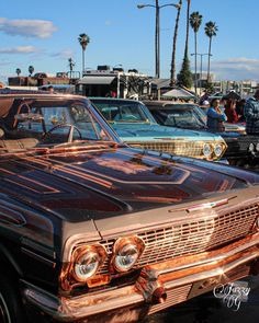 an old car parked in a parking lot next to other cars with palm trees behind it