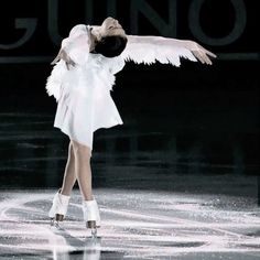 a woman in white is performing on the ice rink with her wings spread out and one leg bent forward