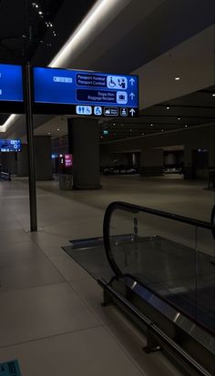 an empty airport terminal with blue signs above the escalator