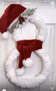 a christmas wreath with a santa hat hanging on the front door and an ornament attached to it