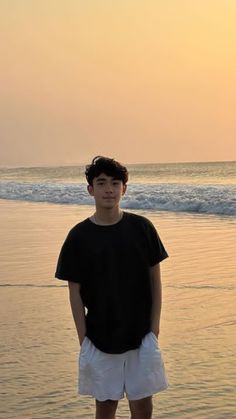 a young man standing on the beach at sunset