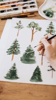 someone is painting trees on paper with watercolors