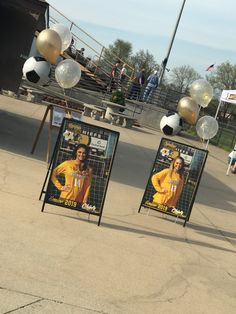 two signs with pictures of women on them in front of some balloons and soccer balls