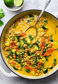 a large skillet filled with curry, meat and veggies next to limes