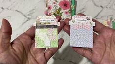 two hands holding small cards in front of a marble counter top with flowers on it