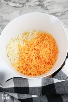 shredded cheese and carrots in a white bowl on a black and white checkered towel