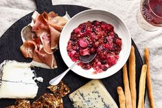 an assortment of cheeses and meats on a black platter with a spoon