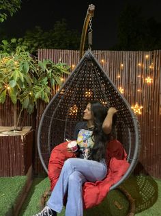 a woman sitting in a hanging chair with lights on the back wall and grass area behind her