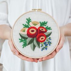 a woman is holding a small embroidery project in her hands, with flowers and leaves on it